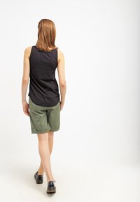 Svart ärmlös topp i kombination med gröna shorts med uppvikta ärmar. Outfiten kompletteras med svarta skor.