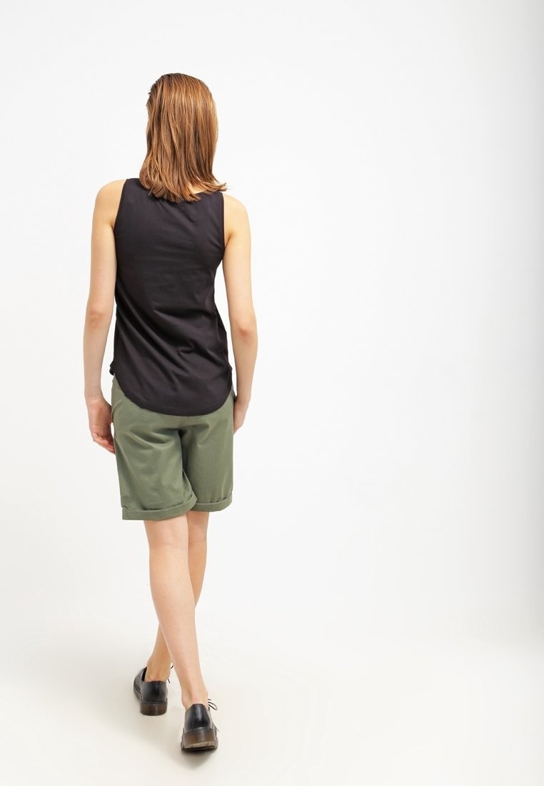 Svart ärmlös topp i kombination med gröna shorts med uppvikta ärmar. Outfiten kompletteras med svarta skor.