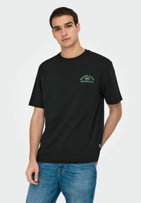 Zwarte katoenen T-shirt met groene tekst die "BEIGEL LANE 24/7 SHOREDITCH" op de bovenste linker borst draagt, in een relaxte pasvorm.