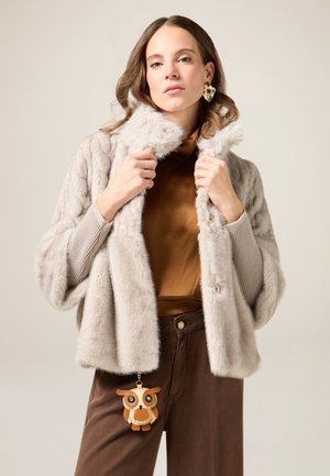 Kunstpelzjacke in Hellgrau mit weiter Kragen, strukturiertem Muster und Knopfverschluss. Braune, hoch taillierte Hose und Eulenschlüsselanhänger als Accessoire.