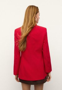 Rdeč blazer z dolgimi rokavi, enostavno silhueto in krojenim dizajnom. Gladek material, minimalistični detajli in brez vidnih okraskov.