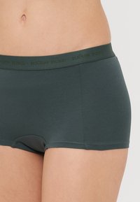 Boxer briefs verde escuro feitos de tecido macio, com uma faixa elástica ampla e discreta com texto da marca e uma textura suave.