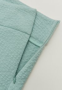 Tissu texturé bleu-vert clair avec un design matelassé, doté d'une fermeture éclair dissimulée et d'un bord lisse le long des bords.