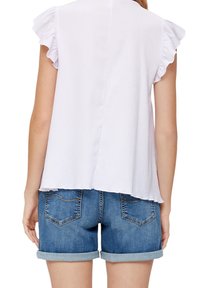 Jasnofioletowa bluzka z krótkimi, falbaniastymi rękawami, teksturowaną tkaniną i linią dołu sięgającą poniżej talii, zestawiona ze złożonymi spodenek dżinsowych.