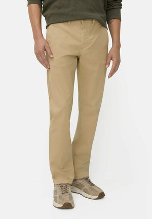 Beige cotton trousers with a straight cut, featuring a button and zip fly, and side pockets. Worn with beige sneakers for a casual look.