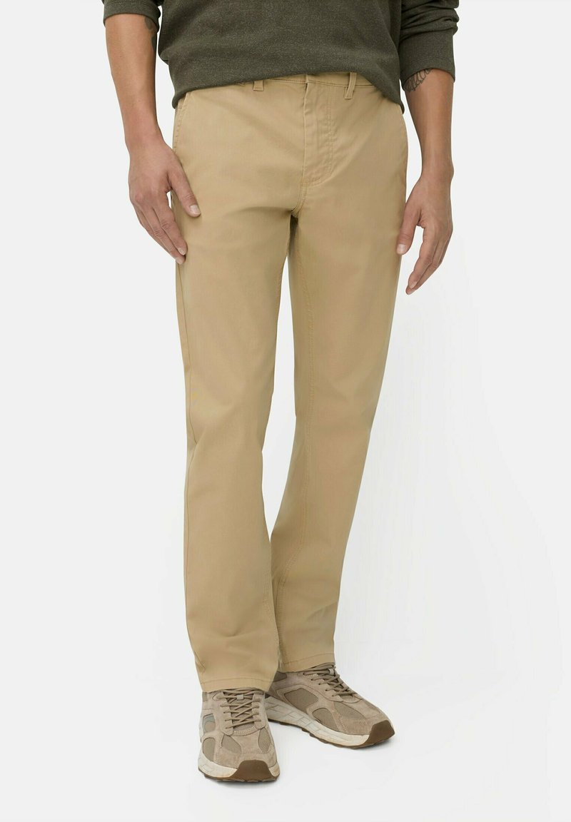 Beige cotton trousers with a straight cut, featuring a button and zip fly, and side pockets. Worn with beige sneakers for a casual look.