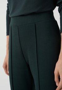 Ciemnozielone spodnie z wysokim stanem z plisami. Wykonane z miękkiego materiału, o gładkiej fakturze i dopasowanym kroju.