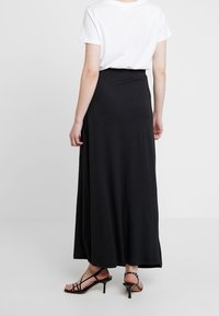 Falda larga negra con una textura suave, cinturilla elástica, diseño fluido y abertura lateral. Combinada con una camiseta blanca y sandalias de tiras.