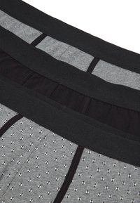 Trois paires de boxers pour hommes empilées, montrant des ceintures noires et des motifs en tissu gris et noir.
