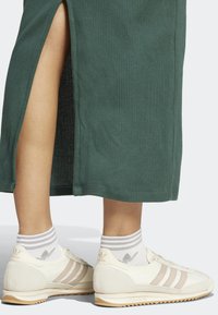 Bílé sportovní boty s béžovými pruhy, nošené s šedě pruhovanými ponožkami, spárované se zelenými žebrovanými šaty s bočními rozparky.