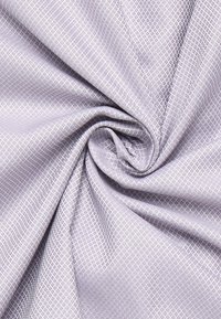 Tessuto lilla chiaro con un design a diamante testurizzato, drappeggiato con grazia, che mette in mostra la sua superficie liscia e la sua qualità flessibile.