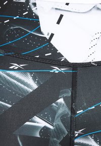 Tissu athlétique noir et gris avec des motifs géométriques et des accents bleus, présentant une texture lisse et des coutures surpiquées.