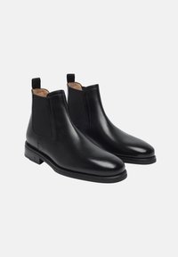 Bottines Chelsea en cuir noir avec panneaux latéraux élastiques, bout rond, texture lisse et talon bas empilé. Comprend des tirettes pour un enfilage facile.