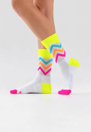 Legs wearing white crew socks with neon yellow cuffs, heels, and pink toes, featuring zigzag patterns in blue, orange, and pink.