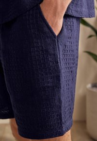 Bermuda azul marino con un patrón texturizado y tejido, y un bolsillo lateral. Fabricadas con material transpirable, presentan un corte recto y un dobladillo.