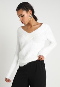 Witte, donzige trui met een V-hals ontwerp, lange mouwen en geribbelde manchetten, gecombineerd met zwarte, gestructureerde broek.