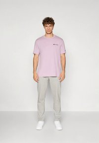 Light purple short-sleeve t-shirt with black logo, paired with light gray tapered pants and white sneakers. Simple and casual design.