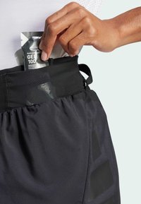 Shorts de sport noirs avec une taille élastique, comportant une poche latérale contenant un sachet de gel. Le matériau est lisse avec une texture mate.