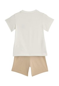 Bawełniany dwuczęściowy strój składający się z białej koszulki z krótkim rękawem i beżowych szortów, oba o miękkiej fakturze i prostym wzornictwie.