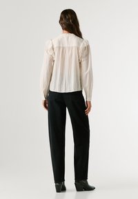 Ilga rankovė kreminė bluzelė su pūkuotomis rankovėmis, švelnus tekstilės audinys, surinktas nugaros dizainas ir apvalus iškirpimas, derinama su juodais tiesiais džinsais.