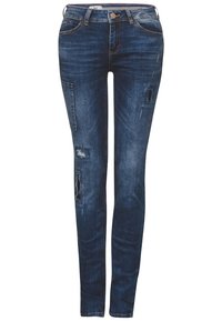 Jeans ajustados en denim azul oscuro con detalles desgastados, incluyendo desgarros y decoloración. Presenta una cintura de altura media y un diseño clásico de cinco bolsillos.