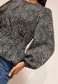 Blusa nera con macchie bianche, con maniche a sbuffo e vita cintrata. Tessuto liscio con una leggera lucentezza.