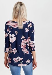Haut bleu marine avec un motif floral en rose et blanc, manches trois quarts, en tissu doux et décontracté. Porté avec un jean bleu clair.