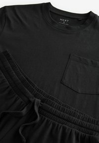 Tricou din bumbac negru cu guler rotund și o buzunar pe piept, asocat cu pantaloni scurți de lounge negri cu talie elastică și cordon.