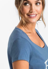 Camicia blu a maniche corte con scollo rotondo, realizzata in un tessuto morbido e leggero, con un design grafico bianco sul petto.