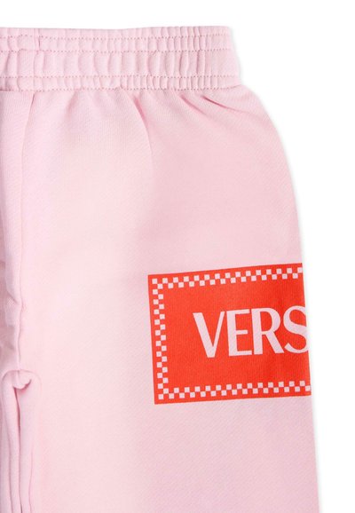 Pantalon de survêtement rose avec une taille élastique, arborant un grand logo rectangulaire rouge sur lequel est écrit "VERS" en lettres blanches. Matière en coton douce.