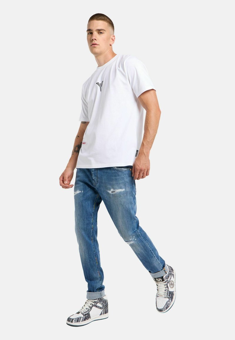 White short-sleeve t-shirt with logo detail, distressed blue jeans, and high-top sneakers featuring a patterned design in shades of blue and white.