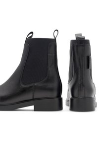 Melni ādas potīšu zābaki ar elastīgiem sānu paneļiem, plakaniem gumijas zole, un cilpas aizmugurē. Gluda virsma ar minimāliem šuvju detaļām.