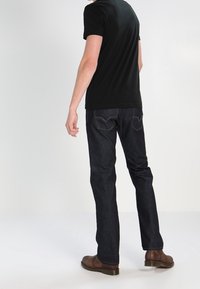 Mörkblå jeans av denim, rak ben-design, kombinerat med en svart kortärmad skjorta och bruna läderstövlar.