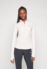 Pullover rosa chiaro a maniche lunghe con collo a metà zip e fori per il pollice, caratterizzato da dettagli logo sottili. Abbinato a leggings scuri.