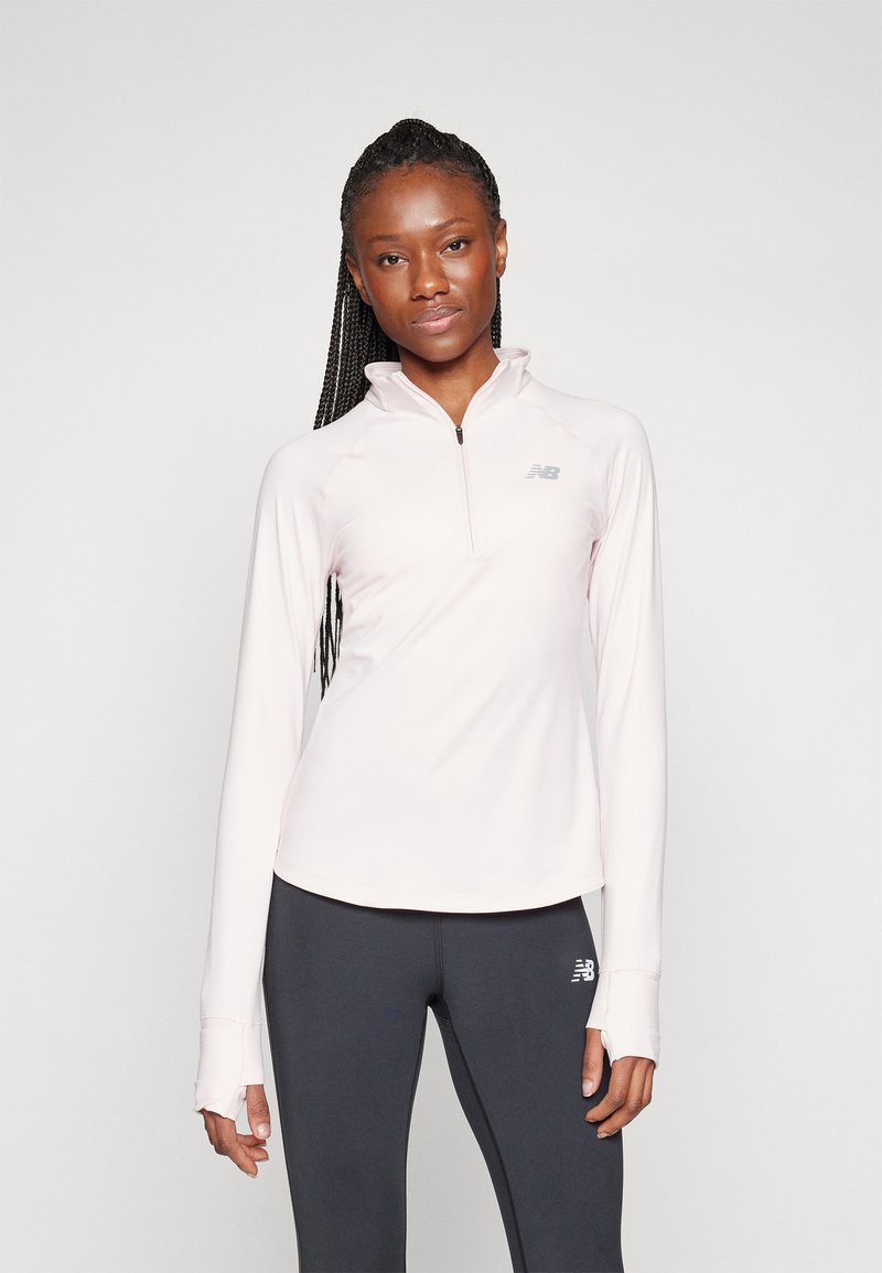 Pullover rosa chiaro a maniche lunghe con collo a metà zip e fori per il pollice, caratterizzato da dettagli logo sottili. Abbinato a leggings scuri.