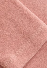 Primo piano di un tessuto in pile rosa che mostra una texture morbida e cuciture fitte lungo il bordo piegato.