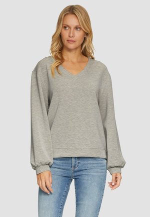 Sweatshirt gris avec un col en V, des manches longues volumineuses et des poignets côtelés. Tissu léger avec une texture douce. Porté avec un jean bleu.