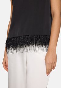 Czarny top z frędzlami z teksturowanych pasm. Gładki materiał na całej powierzchni, zestawiony z jasno kolorowymi, szerokimi spodniami.