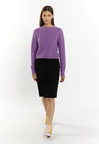 Maglione viola a trecce con maniche lunghe, gonna nera al ginocchio e sneakers arancioni alte su un modello con sfondo bianco.