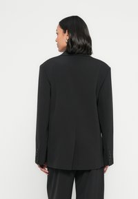 Zwarte op maat gemaakte blazer met gestructureerde schouders, een ventilatie aan de achterkant en knoopmanchetten. Glad stof met een professionele pasvorm.