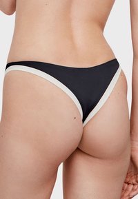 Parte inferior de bikini negra con ribete blanco, que presenta un diseño clásico de altura baja y una textura suave, enfatizando un estilo simple y minimalista.