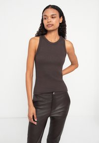 Top din bumbac maro, cu dungi, cu decolteu rotund, design ajustat și fără mâneci, asortat cu pantaloni strălucitori din piele neagră.