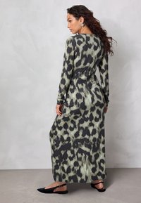 Maxikleid mit langen Ärmeln in grünem und schwarzem Leopardenmuster, mit entspanntem Schnitt, glatter Textur und schwarzen flachen Schuhen.