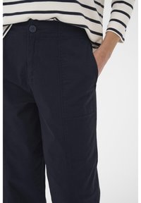 Pantalon bleu marine en coton, avec fermeture à bouton, poches latérales et coupe décontractée. Texture lisse avec un léger éclat.