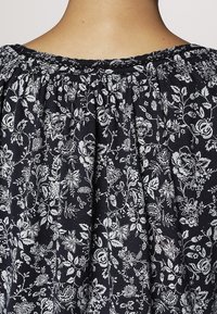 Blusa negra de flores con patrones botánicos blancos, escote elástico, tela fruncida y textura de algodón suave.