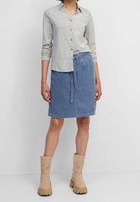 Gray long-sleeve shirt with button closure, pocket. Blue corduroy skirt with drawstring waist. Beige knee-high boots with chunky soles.