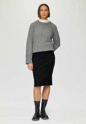 Pull en tricot gris avec ourlet à côtes, associé à une jupe crayon noire. Des bottines noires avec des chaussettes en tricot complètent la tenue.
