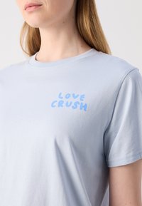 Lyseblå bomulls T-skjorte med rund hals og korte ermer, med teksten "LOVE CRUSH" i en lekende blå skrift på brystet.