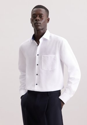 Camicia bianca a maniche lunghe con taschino, dotata di bottoni neri e colletto a fantasia blu navy. Tessuto morbido, vestibilità sartoriale.