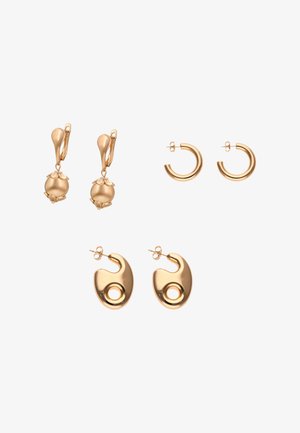 Trzy pary kolczyków w odcieniu złota: u góry po lewej z zawieszonymi kulkami i kwiatowymi nakładkami, u góry po prawej małe otwarte koła, na dole abstrakcyjne owalne kształty z okrągłymi wycięciami.